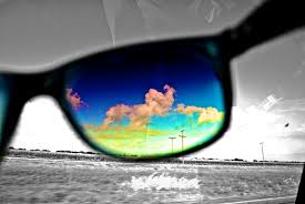 Coloured picture of clouds in the sky through a single sunglasses lens with a grey background